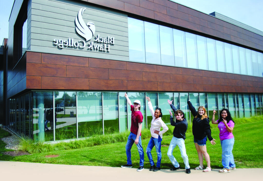 Five students pointing to a new Black Hawk College academic building.